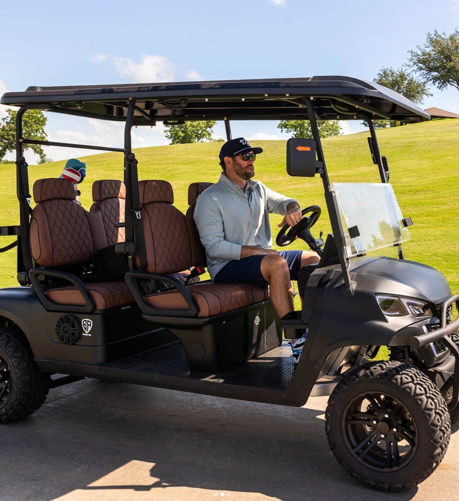 Black EA4F+ 60V four-seat forward-facing lithium electric golf cart with brown quilted seats on a golf course cart path, an adult at the wheel