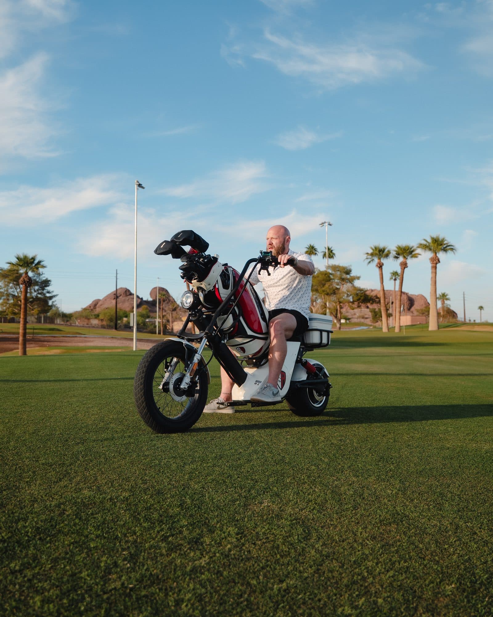 EA Carts Golf Bike, a single-rider 60V lithium electric golf bike in white with a red and white golf bag and cooler, ridden across a fairway lined with palm trees